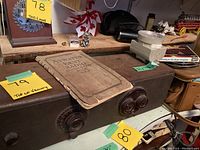 Antique Atwater Kent radio with dials visible, showing the large rectangular radio on a table with a worn instruction booklet on top. Nearby on the shelf are other assorted items.