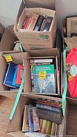 Five boxes filled with an assortment of books including titles by Dan Brown, Candace Bushnell, Kate Adie