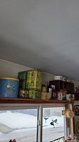 Wide view of collectible tins, bowls, and cups above a window shelf, showing items for sale in lot.