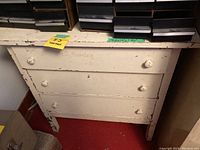 Front view of cream-colored wooden dresser showing three drawers with round knobs. Noticeable wear with chipped paint and scratches.