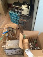 Overview showing vintage electric churn with glass container, electric griller, milk crate, and boxes of utensils and kitchen tools