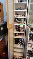 Tall cabinet with shelves filled with light fixtures, bulbs, broom, and other small items.