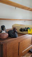 Full lot showing two wooden mallard carvings and boxed wooden roadster model car on wooden cabinet.