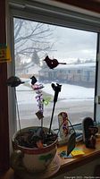 Window sill with plant pot holding stained glass butterfly and cross stakes, also visible small figures and fly swatters.