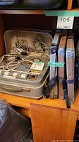 Shows the tape recorder in a carrying case with power cord and accessories, plus three reel wheels in boxes and one reel wheel attached to a metal frame with straps