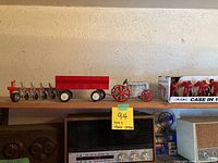 Shelved red tractor toy with attached trailer and Case IH 1840 Cultivator toy implement displayed in box.