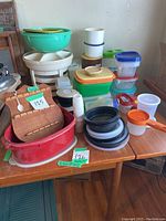 Wooden spoon rack with collectible spoons and a stack of assorted plastic Tupperware containers along with plasticware items on a table.