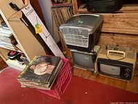 Three vintage CRT TVs, microphone boom stand box, and vinyl album crates shown on floor near wooden furniture.