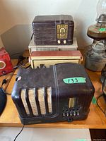 Four vintage radios shown on wooden table with varying sizes and designs. Smallest radio has a cracked housing. Power cords visible but some incomplete. Includes radios with slider controls and knob tuning