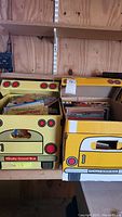 Two yellow cardboard boxes designed like school buses filled with children's books arranged on a wooden shelf.