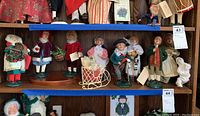 Front view of 11 Byers Choice Christmas caroler figurines on wooden display shelves, showing variety of clothing and accessories.