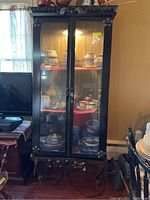 Full front view of black metal china cabinet on decorative base with interior light on