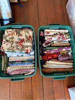 Two green plastic tubs filled with assorted folded and rolled fabric pieces with floral prints and various patterns.