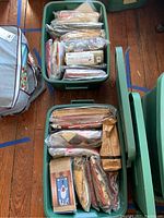 Two green plastic bins filled with folded fabric pieces and quilt kits in sealed plastic bags