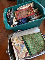 Green plastic bin filled with assorted fabrics and quilt kits along with a fabric storage bag with folded fabric inside