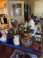 Table display of assorted pottery, glassware, and decorative items including teapot, candle holders, steins, and figurines.