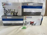 Four boxes of Moda Concept stemless wine glasses, each box containing 4 glasses, totaling 16 glasses. Boxes labeled with glass capacity and type (red or white).
