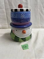 Front view of closed ceramic snowman cookie jar with segmented lid and colorful decoration including green scarf and carrot nose