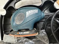 Close-up of Black & Decker Mouse hand sander/polisher placed inside the case with attached sanding pad and power cord visible.
