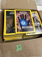 Opened cardboard box filled with National Geographic magazines, stacked neatly showing covers including 'The Future of Medicine' issue