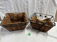 Two garden baskets with metal frames and coco liners side by side, showing one without hanging chain and one with hooks for hanging.