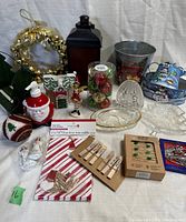 Overview of various Christmas decorations including a metal bell wreath, lantern, Santa soap dispenser, figurines, ornaments, glass dishes, tins, clothespins, and treat bags.