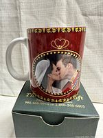 Front side of the mug showing Prince William and Catherine Middleton kissing in wedding attire, set against a red background with gold heart pattern trim along the top.