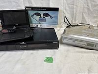 Lot showing Sony portable DVD player with power adapter, Panasonic Blu-ray player, silver under-counter disc player, and D-Link monitor switch box and cable.