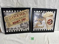 Set of two framed movie theatre-themed prints showing cinema ticket and popcorn images, displayed side by side.
