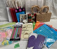 Photo showing several paper gift bags of different patterns and sizes, packaged colorful plastic goodie bags, and gift tags on a white cloth background