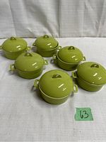 Set of six bright green ceramic bowls with lids arranged in two rows on a white fabric surface.