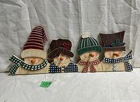 Full frontal view of the wooden snowman coat hooks set showing all four snowmen heads, their hats, scarves, and carrot-shaped nose hooks.