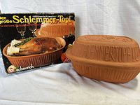 Vintage brown clay roasting pot and lid with embossed rooster design sitting next to original box showing cooking example.