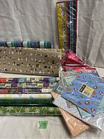 Photo showing various rolls and folded sheets of vintage gift wrap primarily featuring dog motifs, geometric patterns, and sports themed blue sheets