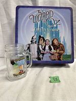Image showing The Wizard of Oz Trivia Game metal tin and a glass drinking mug with Dorothy's shoes illustration.