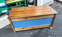 Closed side view of wooden storage box with brown wood frame and blue painted front panel on wheels.