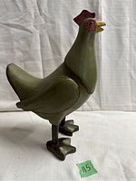 Front left view of wooden chicken figurine showing green paint with red comb and yellow beak.