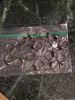14 assorted costume jewelry rings arranged on a clear plastic bag on a dark marble surface for condition and detail visibility.