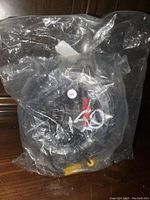 Coiled black cable inside clear plastic packaging with visible connectors including yellow RCA and power connectors.