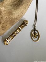 Top view of antique gold filled bar brooch with geometric design and oval pendant necklace with flower charm on chain, placed on white surface next to wooden object.