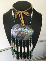 Front view of large abalone shell pendant necklace on black display bust, showing iridescent shell and bead details.