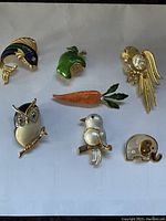 Top-down view of front side the 7 brooches arranged on a white surface showing color and design details.