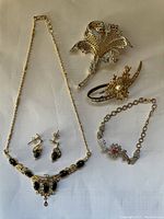 Overview of all five jewelry pieces laid out on a white background including necklace with matching earrings, pearl brooch, floral brooch, and heart motif bracelet