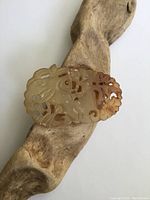 Front angle view of the beige and brown jade pendant showing detailed pierced carving and organic shapes.