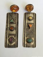 Front view of both silver dangle earrings showing various inset stones and amber tops against white background.