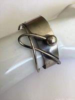 Front angle showing wide silver band, curved wire design and raised ball detail on the cuff bracelet worn on a mannequin hand.