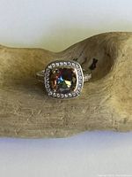Front view of the sterling silver ring with a cushion-cut mystic topaz center stone surrounded by clear crystals on a wooden display.
