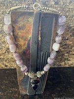 Front view of the necklace displayed on a stand, showing the purple stones and silver-toned pendant with two faceted stones.