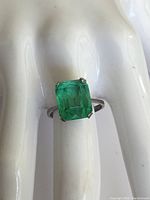 Front view of the ring on white hand form, showing the rectangular green stone and silver band.