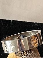 Photo showing silver tone ring with engraved scripted logo and circular emblem design detail.